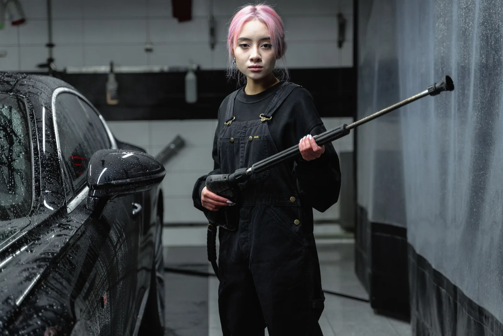 Asian woman with pink hair using a pressure washer at an indoor car wash. What a Pressure Washing Contract Needs Before You Send a Quote