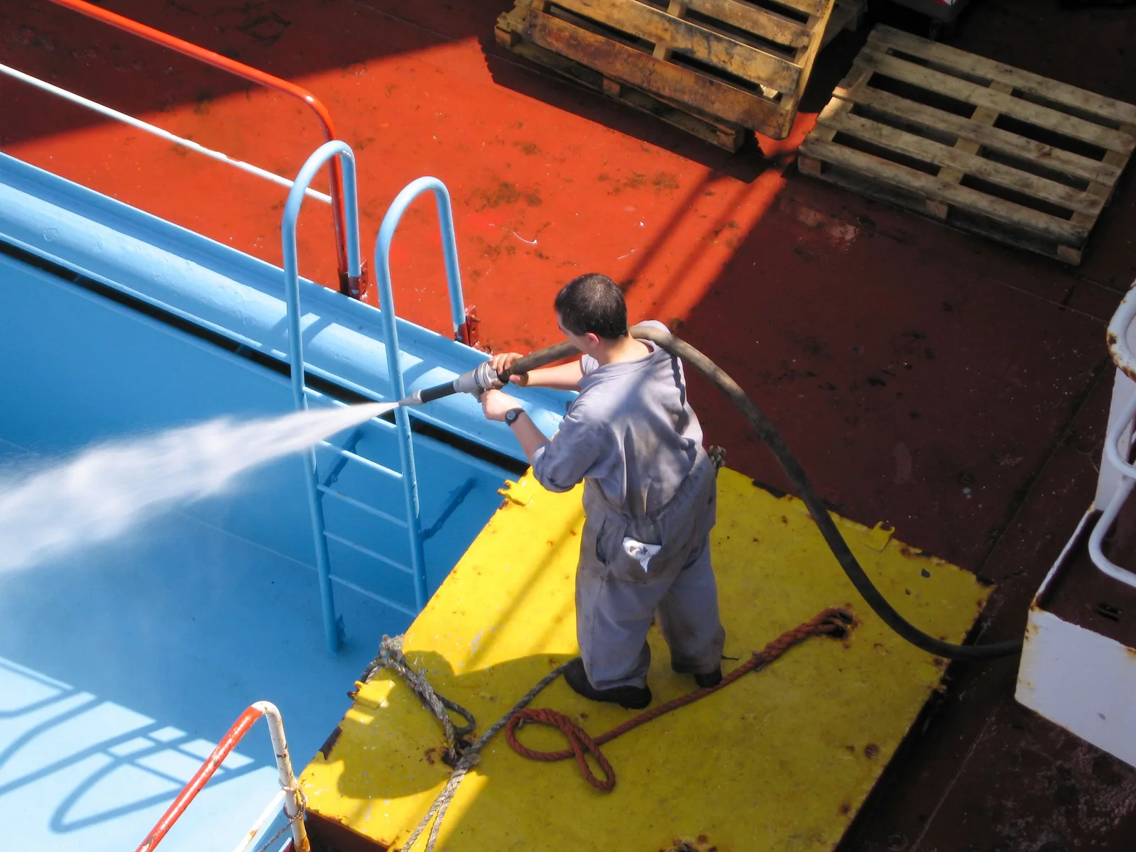 A worker using a high-pressure hose to clean the deck of a ship, showing industrial processes. Do Pressure Washing Customers Need to Sign a Liability Waiver?