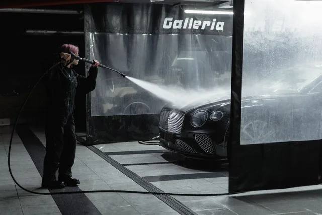 A woman power washing a luxury car in an indoor garage setting, showcasing car wash service. Pressure Washing Quote Template for Small Operations