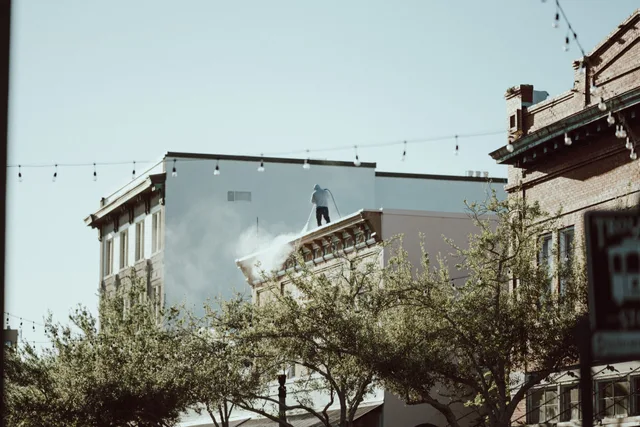 Rooftop worker using pressure washer in a cityscape with urban street below. Pressure washing software: what to record and review