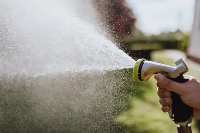 A close-up of a hand spraying water with a hose in a garden setting, perfect for gardening themes. Pressure washing startup: five variables that decide a job