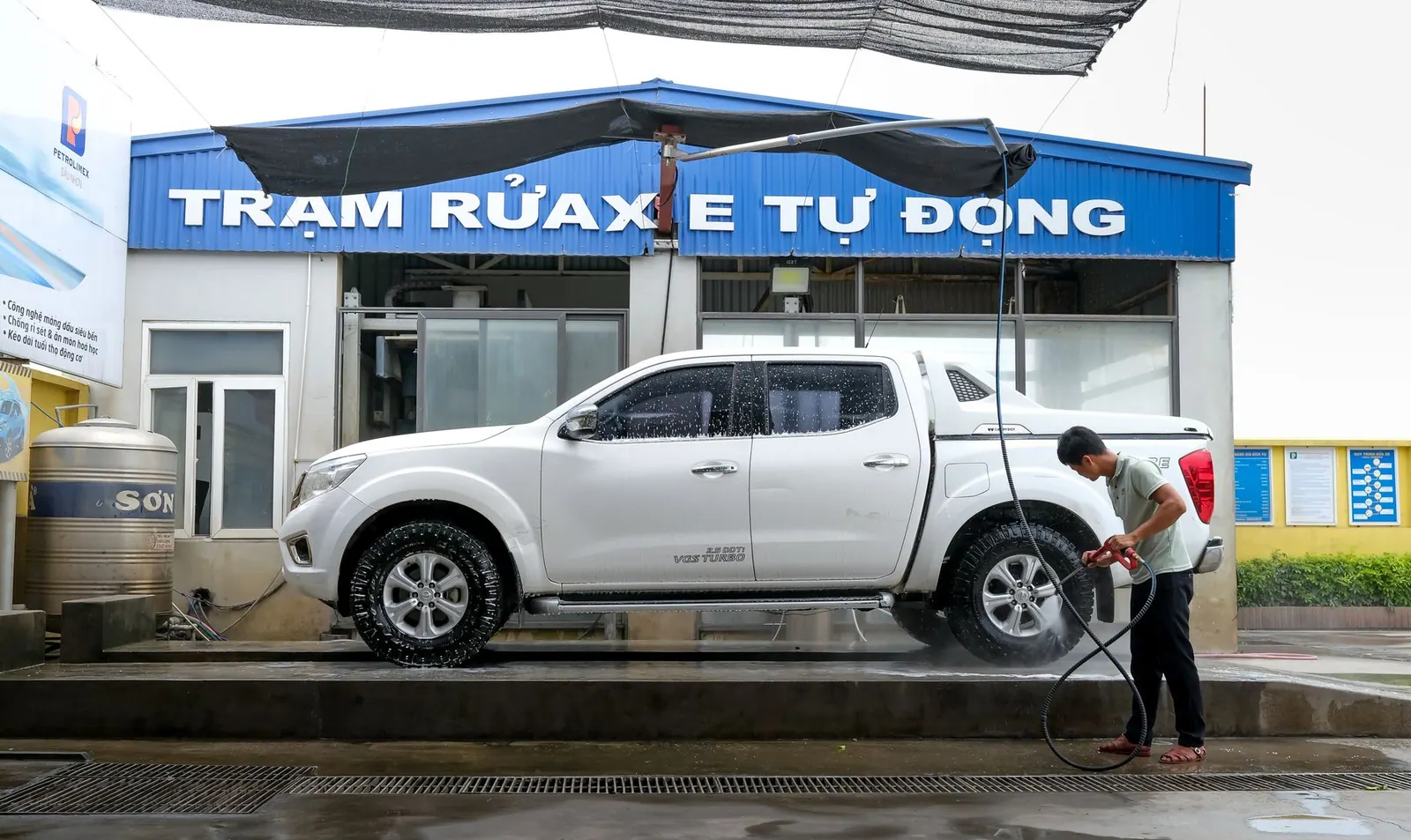 Man cleaning white pickup truck at automated car wash with pressure washer.